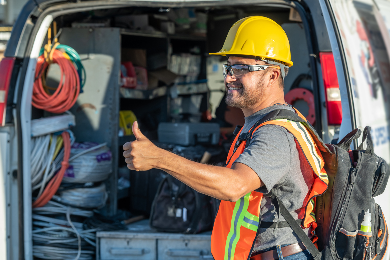 Smiling hispanic construction worker wearing a work helmet looking away with his thumbs up